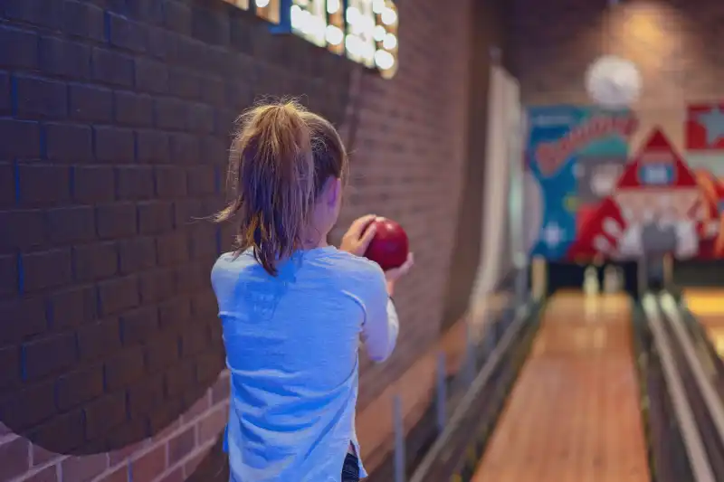 Young brown haired girl with pony tail playing a game of indoor bowls